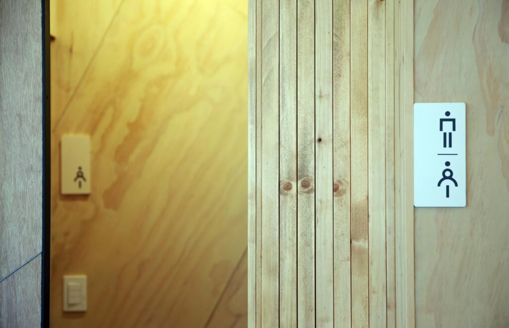 Contemporary wooden bathroom door with gender-inclusive signage in minimal design.